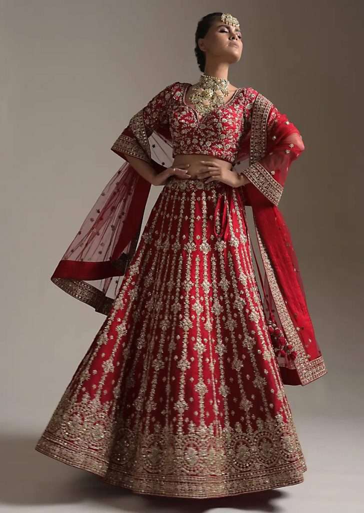 A Women Posing for Photo Wearing Scarlet Red Lehenga Choli In Raw Silk Zari And Resham Embroidered Floral Motifs In Vertical Stripes