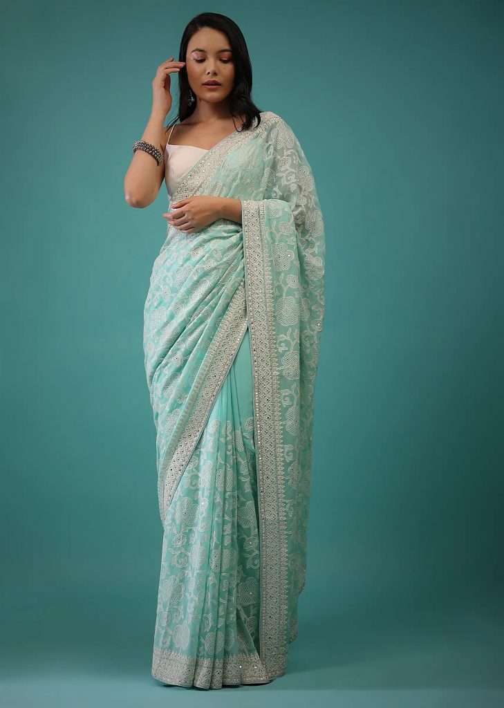 A woman photographed wearing a mint green Lucknowi saree with mirror work, white beads embroidery buttis