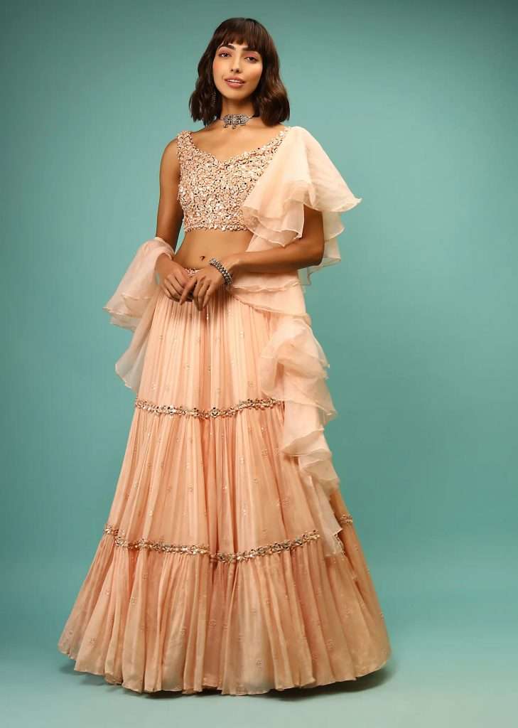 A woman wearing a peach lehenga and crop top set with 3D mirror abla embroidery and ruffled dupatta poses for a photo