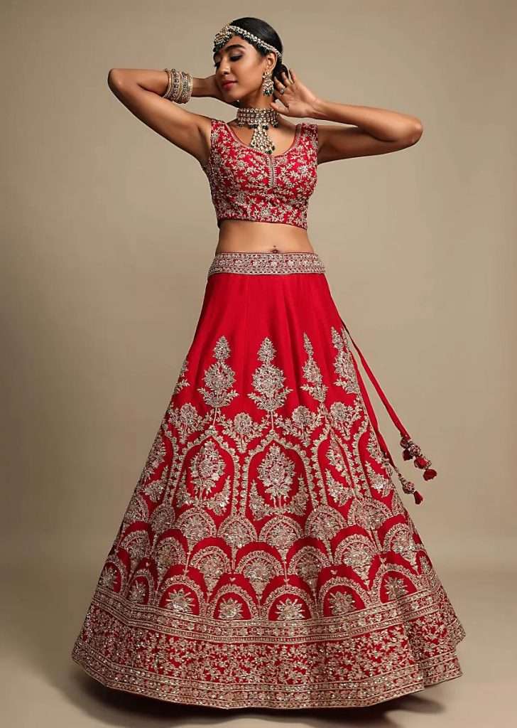 A woman poses for a photo wearing a scarlet red lehenga choli in raw silk with zari embroidered heritage floral kalis