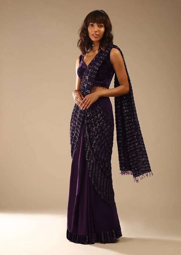 A woman in a wine purple ready pleated saree with striped sequin pallu and matching velvet blouse with bead tassels