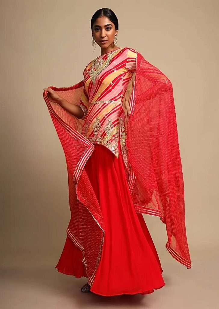 A woman posing for a photo wearing a tomato red skirt and multi color lehariya printed kurti adorned with gotta patti work