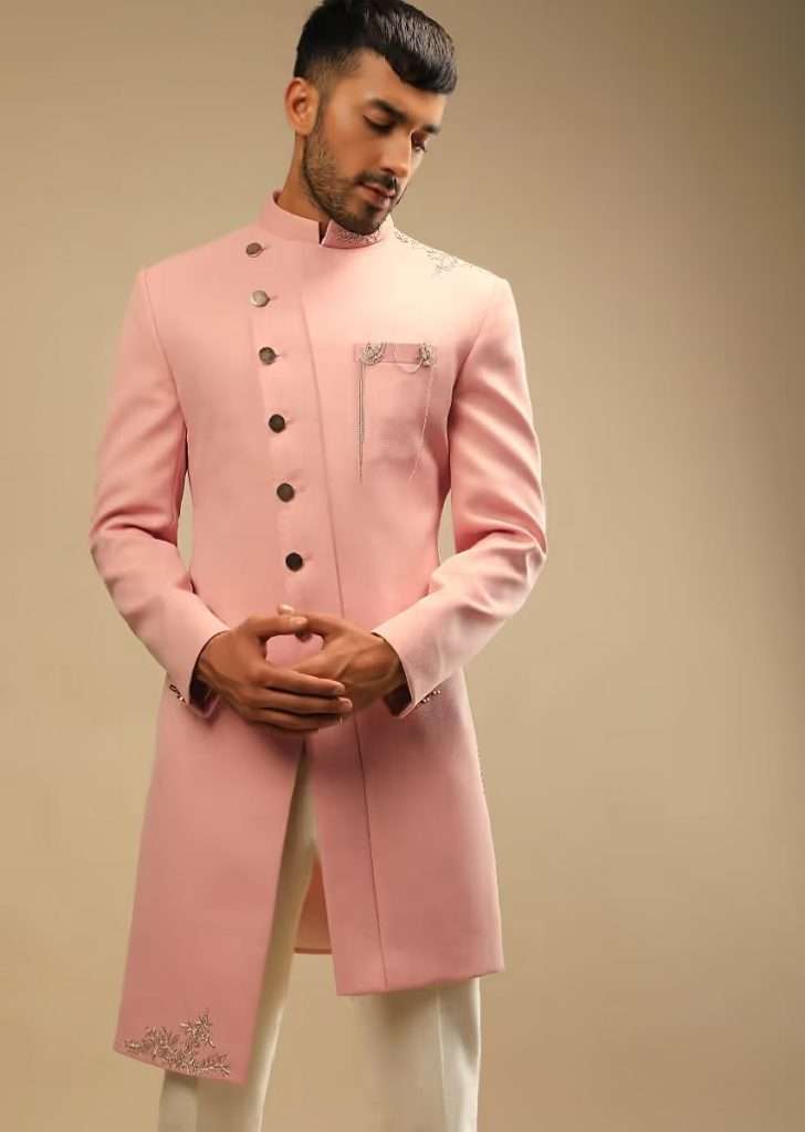 A man poses for a photograph wearing a blossom peach jacket in terry rayon with zardozi embroidered floral motifs and Aligarh pants