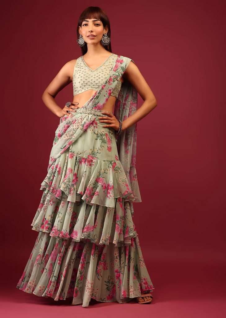 A woman poses for a photo in a green floral printed pleated lehenga saree with an embellished blouse in a layered frill pattern.