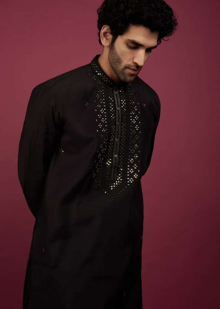A man in a black silk kurta with mirror work on the yoke is posing for a picture
