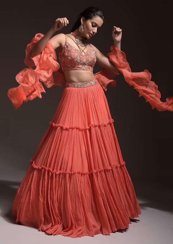 A woman wearing a katdana embellished floral blossom and ruffle dupatta poses for the photo wearing a coral tiered skirt and crop top