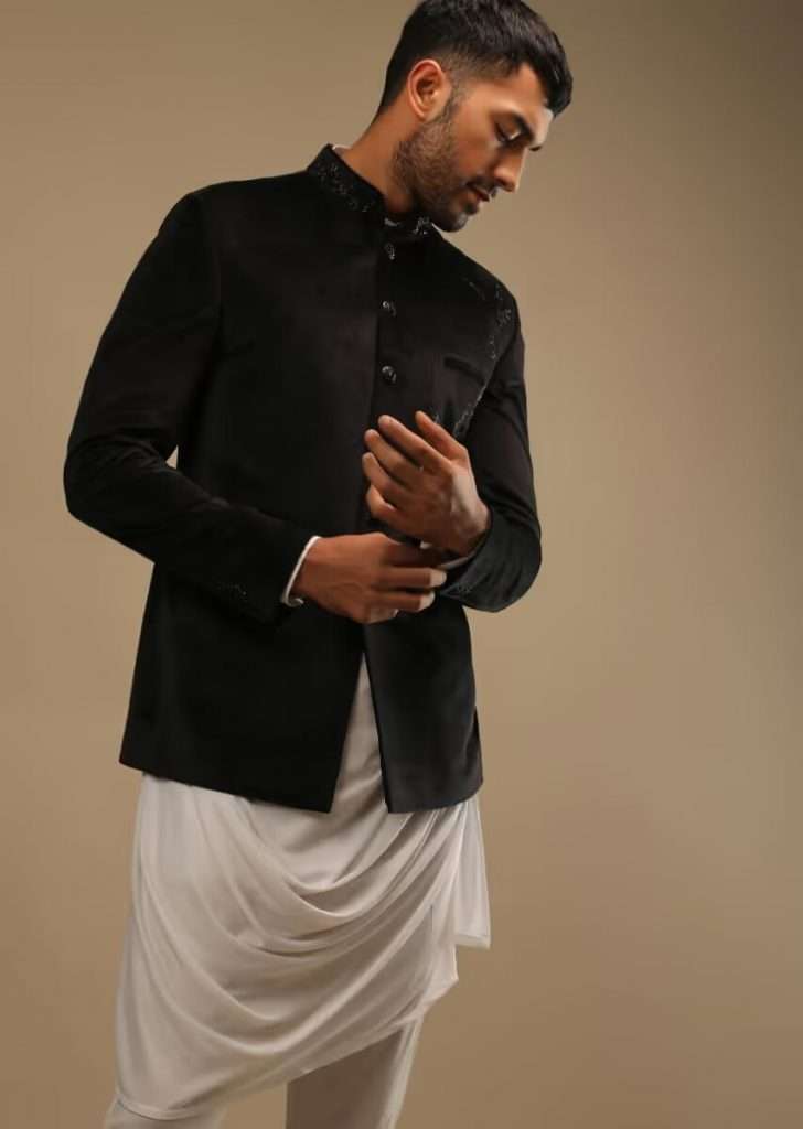 A man wearing black sherwani in velvet with self colored cut dana work and white cowl kurta set is posing for a picture