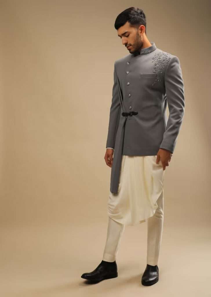A man wearing a frost gray jacket with asymmetric hemline and cream pleated kurta set poses for a photo