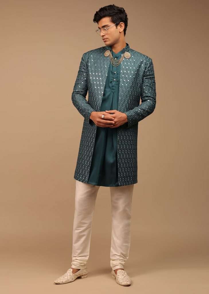 A man wearing an ocean blue sherwani with elaborate thread and abla work poses for a photograph
