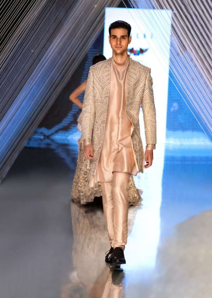 A man wearing a pink sequin embroidered jacket and kurta poses for a photo