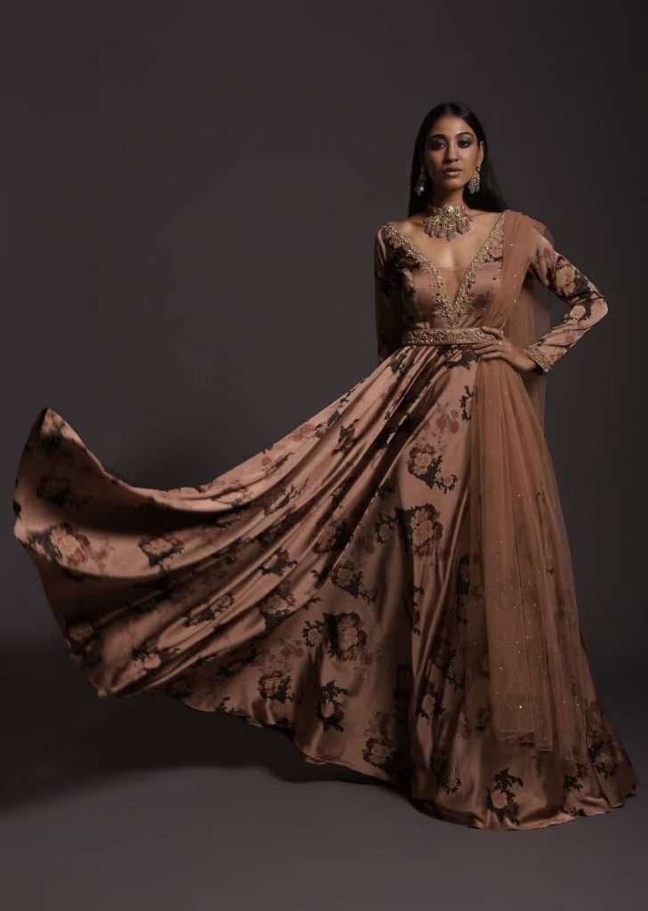 A woman wearing a copper peach anarkali suit with floral print, plunging neckline and an embellished belt is photographed in Milano