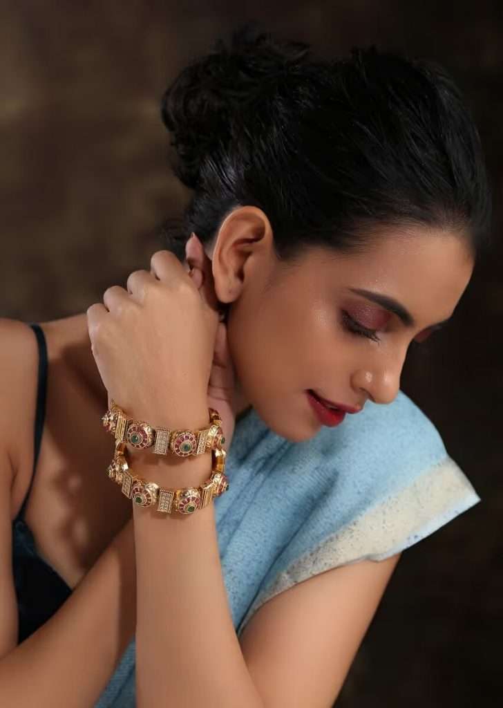 A Women Posing for Photo Wearing Gold Plated Kundan Bangles With Pink And Green Stones And Embossed Temple Work By Paisley Pop