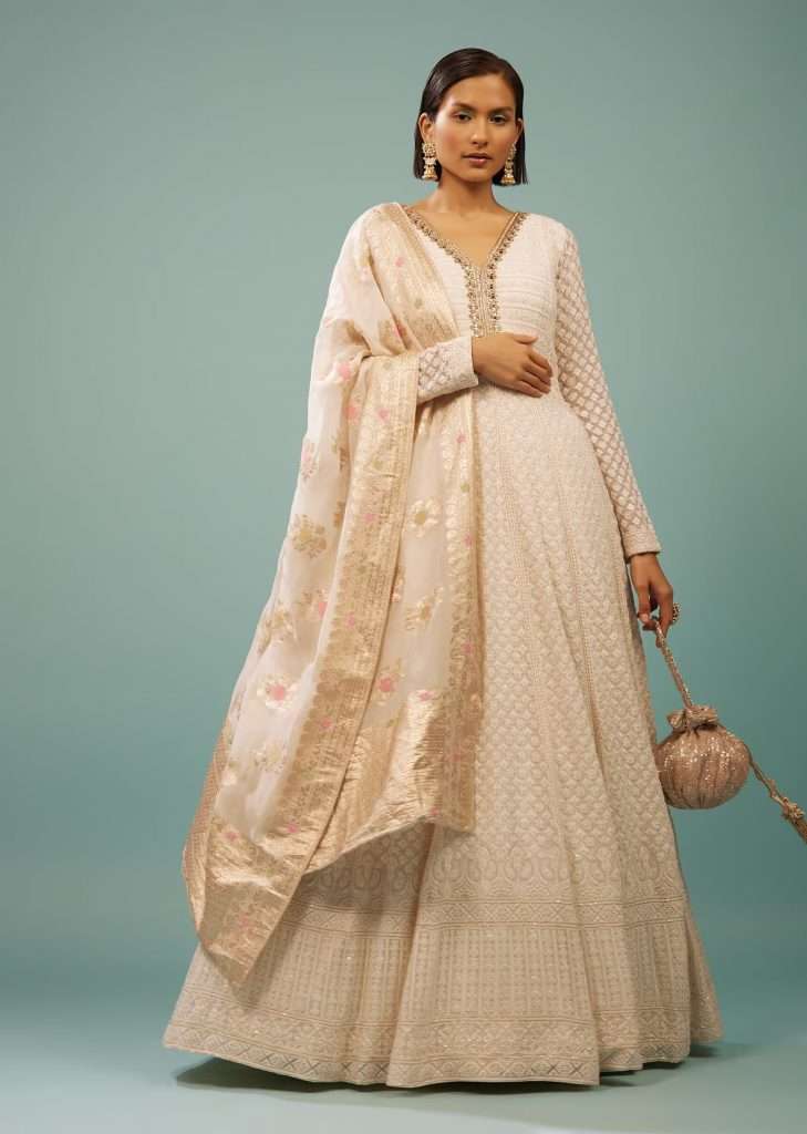 A woman in a white Lucknowi anarkali suit with embroidered georgette poses for a photo