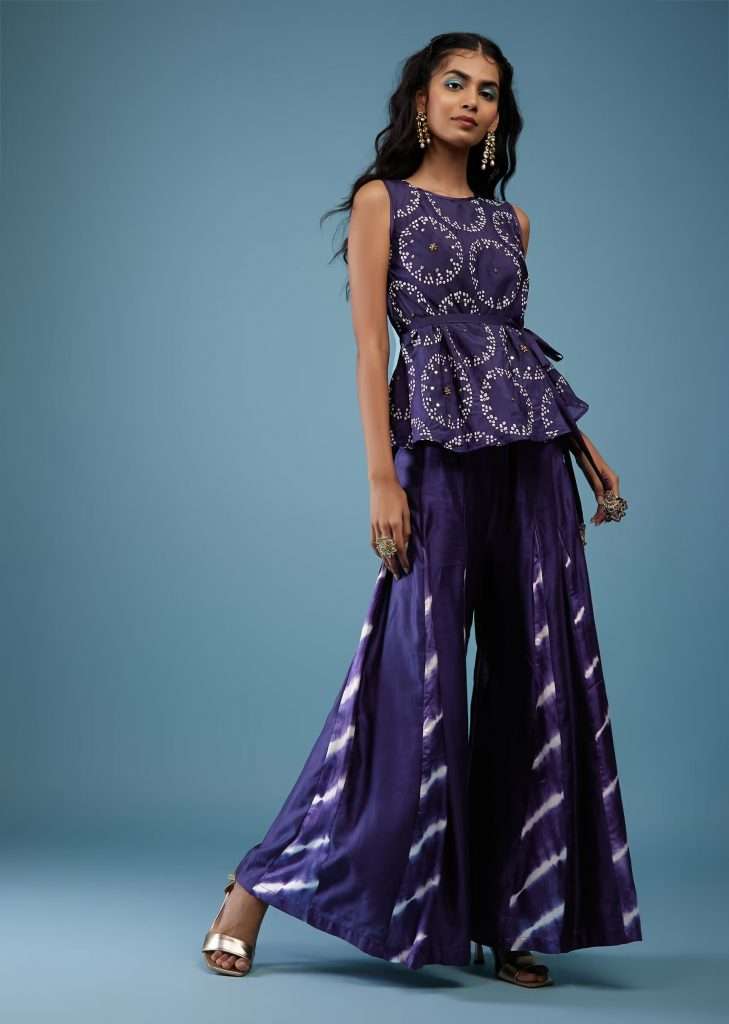A woman wearing a medieval blue bandhani print peplum top with blue tie-dye palazzo poses for a photo