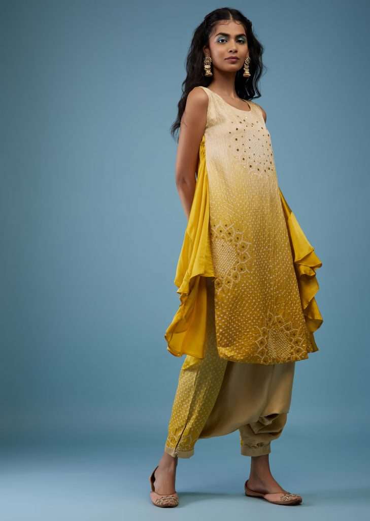 A woman wearing ombre shade beige and golden yellow bandhani tunic top in gajji silk with printed silk cowl dhoti poses for a photograph