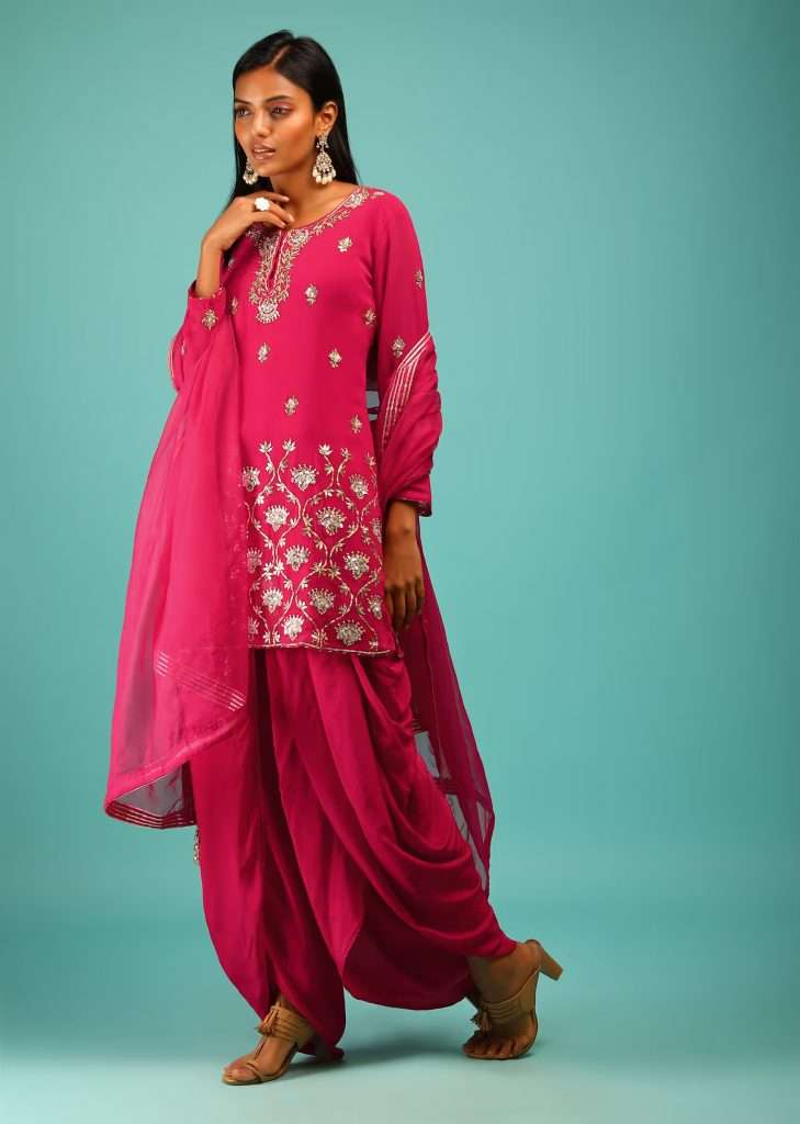A woman wearing a Rani pink dhoti suit with gota patti and embroidered sequins of Moroccan and floral motifs poses for a photo