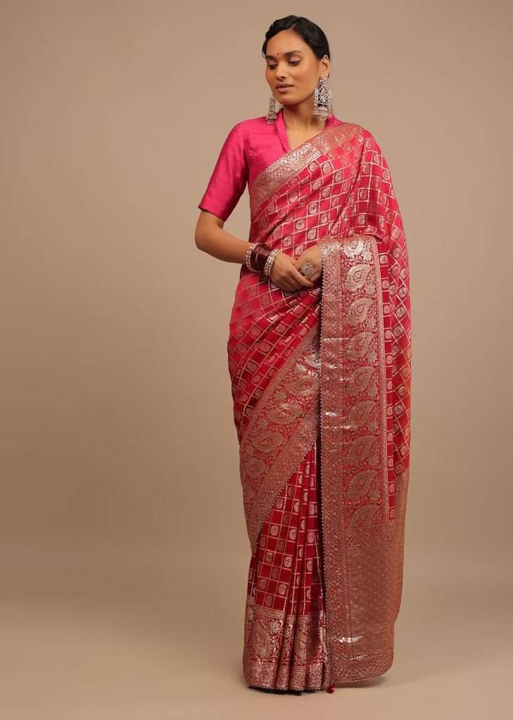 A woman wearing a Rani pink, red and orange ombre saree in silk with lurex woven checks and paisley motifs poses for a photograph
