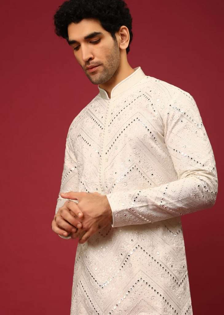 A man posing for a photo wearing a white kurta in raw silk heavily embroidered in floral and chevron designs with silk and mirror embroidery