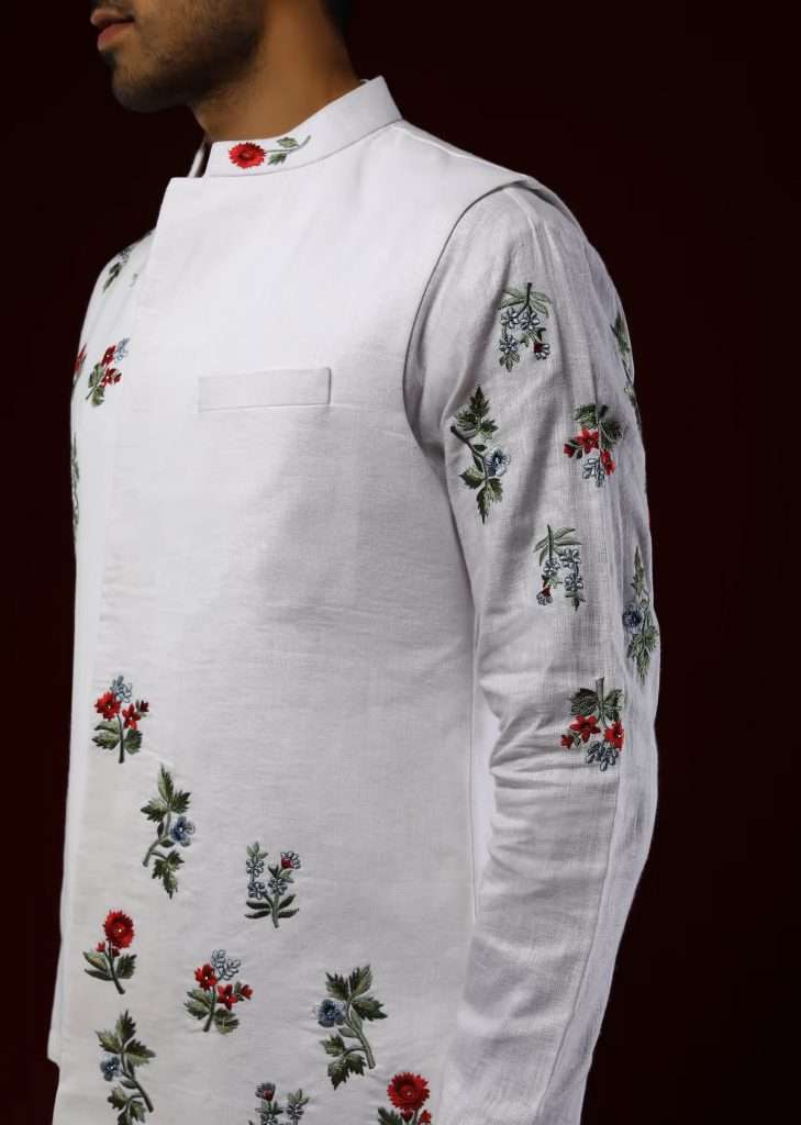 A man wearing a white Nehru jacket set in linen with multicolored silk embroidered floral motifs poses for a photograph