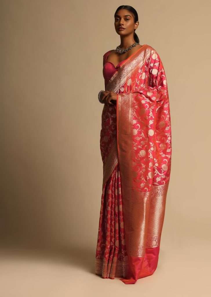 Women posing for photo wearing Coral Pink Two Toned Banarasi Saree In Pure Handloom Silk With Woven Floral Jaal And Floral Border Along With Unstitched Blouse Piece